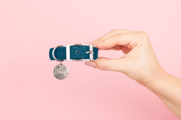 A close-up photo of a person holding a dark blue waterproof dog collar with a silver buckle.